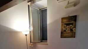 Quarto com sofá vermelho, luminária de chão, janela com persianas e quadro pendurado na parede.