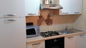 Cozinha compacta com armários brancos, micro-ondas, fogão a gás e forno embutido.