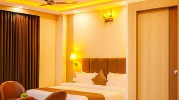 A hotel room with a bed, a desk, chairs, a ceiling fan, and a door.