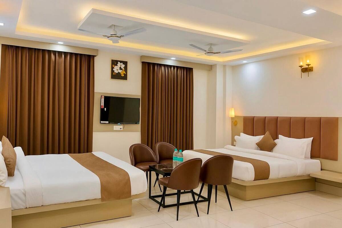 A hotel room with two beds, a TV, a table with chairs, and a ceiling fan.