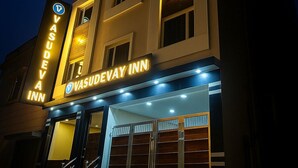 Ein Gebäude mit einem Schild für Vasudevay Inn, das eine moderne Fassade mit zahlreichen Fenstern und einen markanten Eingang mit Glastüren zeigt.