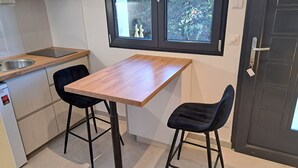 A small kitchen with a wooden table, two black chairs, a black door, and a window with a view of greenery. - Studio Cécilia (Aix-les-Bains)