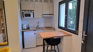 A compact kitchen with a Bosch refrigerator, a microwave, and a sink. There's a small table and a chair, and a window providing a view of greenery outside. - Studio Cécilia (Aix-les-Bains)
