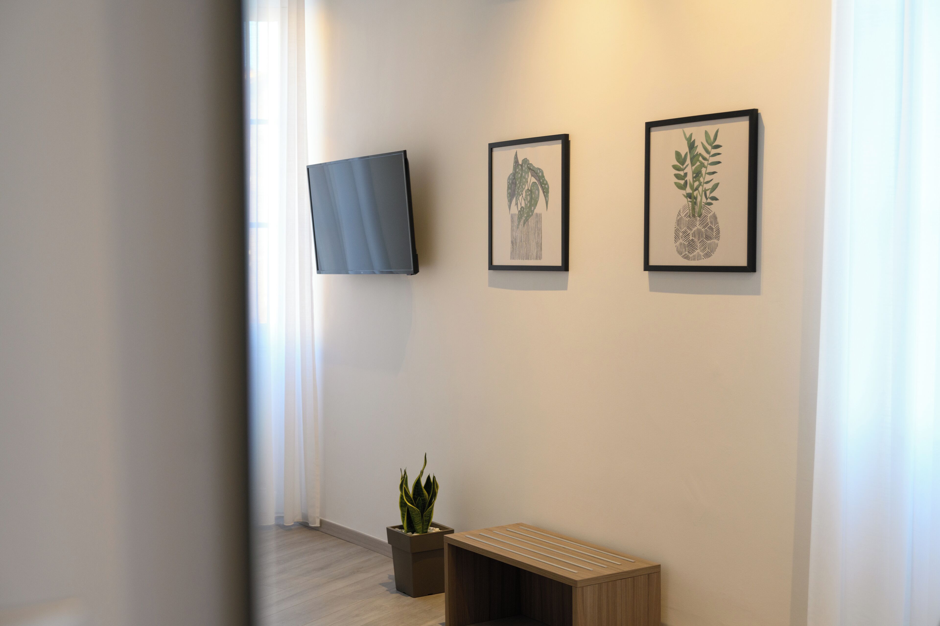 Een hal met een flatscreen-tv aan de muur, twee ingelijste botanische prints, een potplant en een houten bankje.