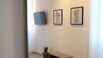 Een hal met een flatscreen-tv aan de muur, twee ingelijste botanische prints, een potplant en een houten bankje.