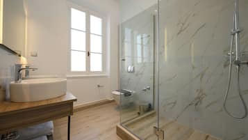 Un bagno moderno con doccia vetrata, lavandino bianco e finestra che permette l'illuminazione naturale.