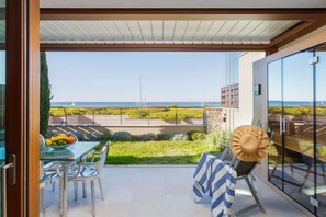 A balcony with a glass door, a table with chairs, a hat, and a view of the sea.