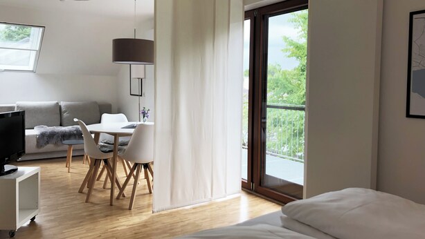 A modern hotel room with a bed, a desk with a chair, a sofa, and a TV.