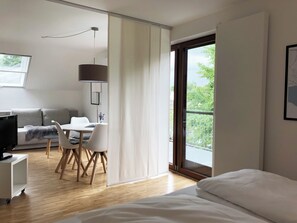 A modern hotel room with a bed, a desk with a chair, a sofa, and a TV.
