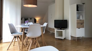 A modern living room with a dining area, a flat-screen TV, and a white cabinet with shelves.