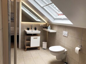 A modern bathroom with a skylight, a sink with two black soap dispensers, a toilet, and a small wooden cabinet.