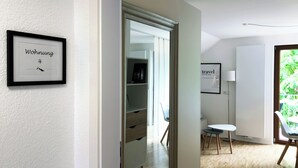 A modern, well-lit room with a wooden floor, a white wardrobe, a small table with two chairs, and a framed picture on the wall.