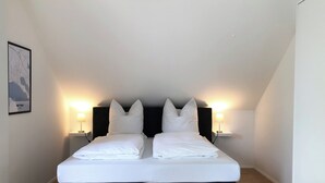 A neatly made double bed with white linens, two black headboards, and two bedside lamps.