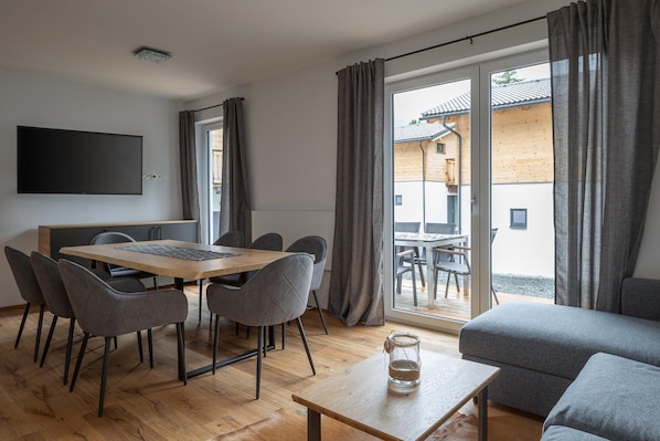 Una sala de estar moderna con un sofá, una mesa de comedor con sillas y un televisor montado en la pared.