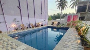 En swimmingpool med ett rutmönstrat kakel runt kanten, omgiven av solstolar och krukväxter.