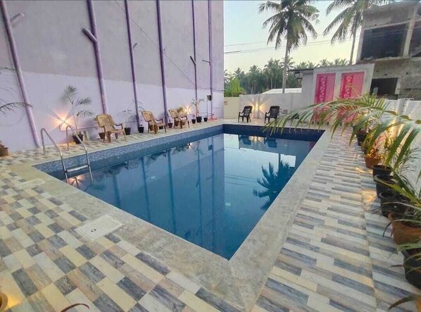 A swimming pool with a checkered tile border, surrounded by lounge chairs and potted plants. - AP Heaven Villa (Vanur)