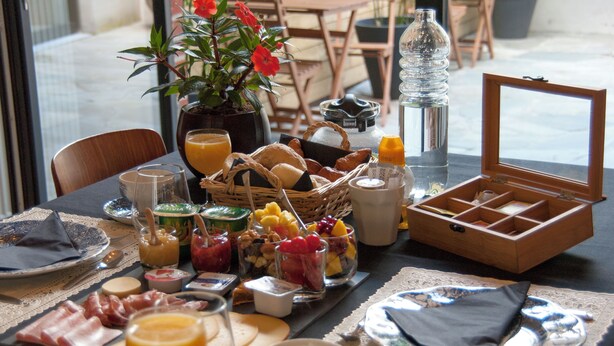 Uma mesa de café da manhã com diversos alimentos, bebidas e uma cesta de frutas.