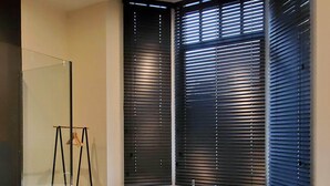 A modern bathroom with a freestanding bathtub, a glass shower enclosure, and large windows with blinds. - OYO  (Kortrijk)