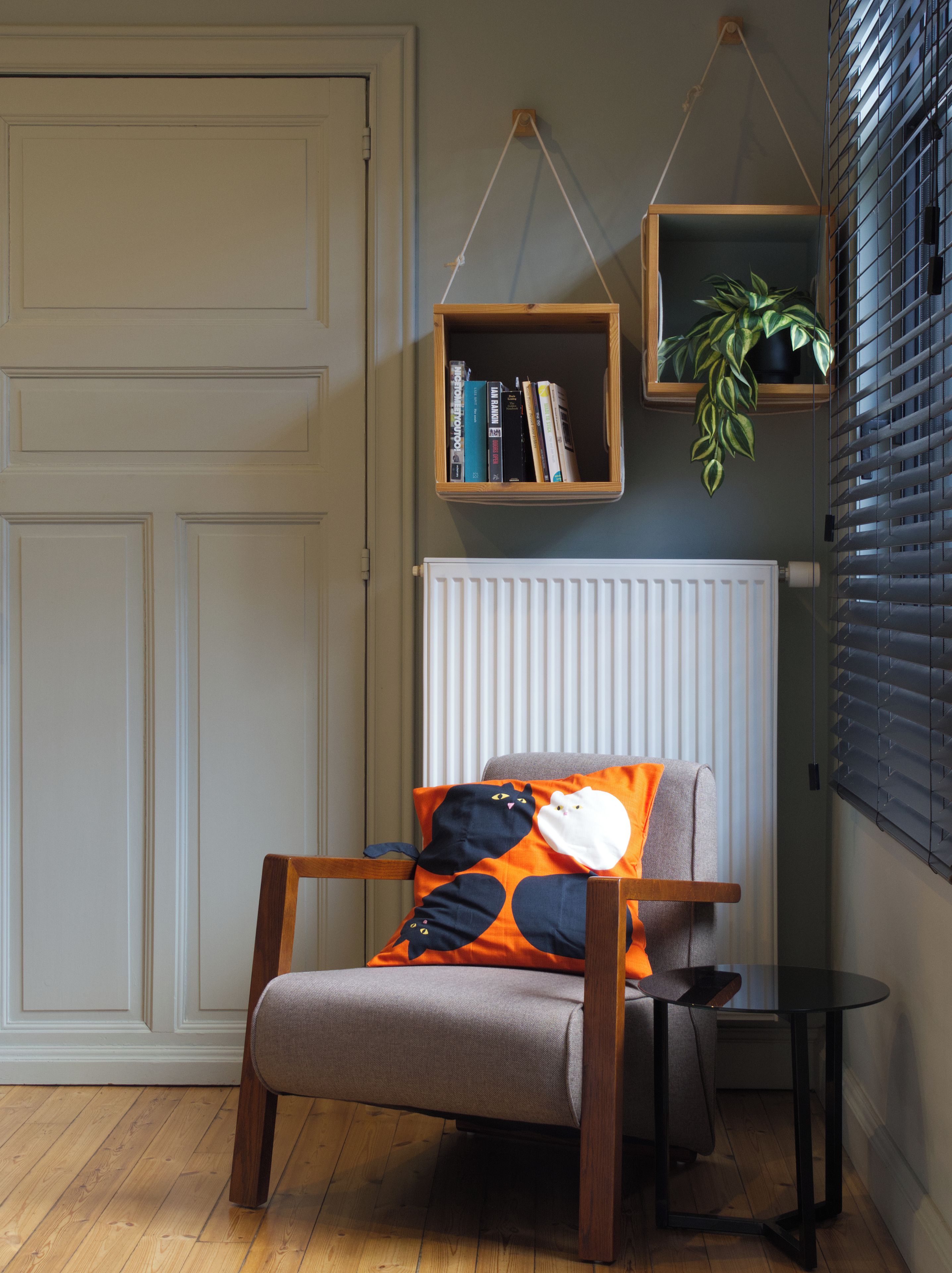 A room with a wooden chair, a radiator, a small table, and bookshelves with books and a plant.