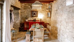 Un comedor rústico con paredes de piedra, vigas de madera, una lámpara de fibra y una mesa dispuesta para cuatro comensales.