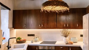 Una cocina moderna con armarios de madera oscura, encimera blanca, estufa integrada y una lámpara colgante de fibras naturales.