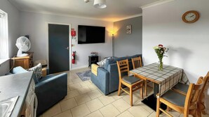 Un salon moderne avec un canapé, une table à manger et des chaises, un téléviseur fixé au mur et une horloge.