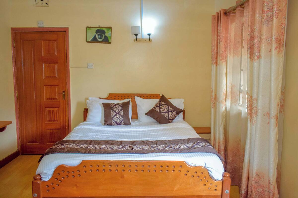 Une chambre à coucher avec un lit en bois, une porte, une lampe fixée au mur et un rideau.