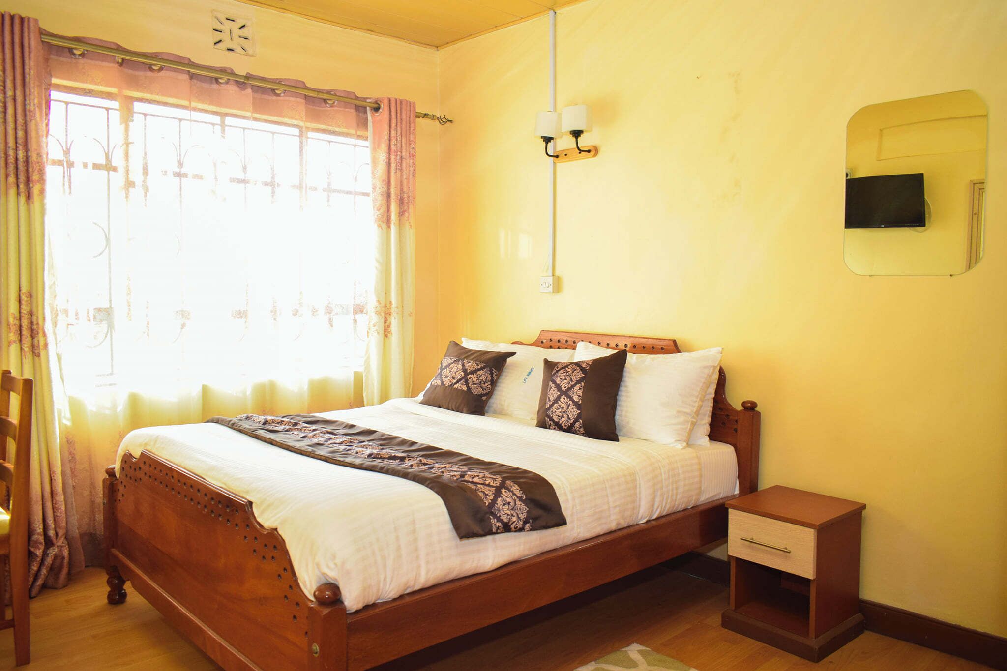 A neatly made bed with a wooden headboard, a bedside table with a drawer, and a wall-mounted light fixture.
