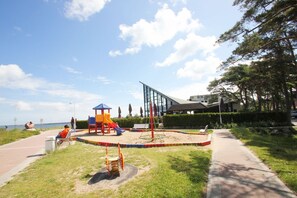 A playground with slides and swings, a paved path, and a building in the background. - Vacation home Strandfeeling Glowe - House in a great location with garden, terrace and (Glowe)