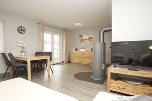 Habitación de hotel moderna con cama, escritorio con televisor, zona de comedor con sillas, pequeña cocina y un ventanal grande.