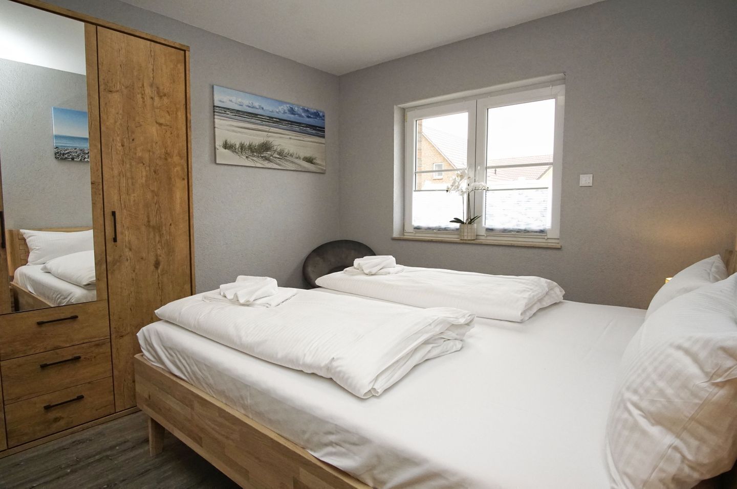 Ein Schlafzimmer mit zwei Betten, einem Holzschrank, einem Fenster mit Aussicht und einem Bild an der Wand.