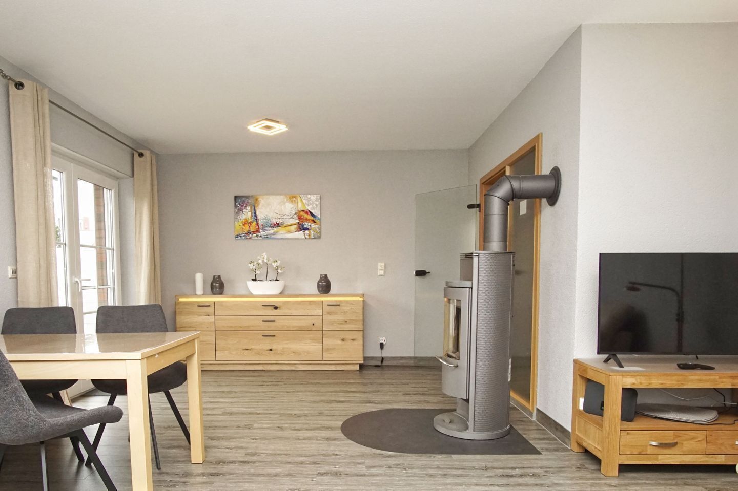 A modern living room with a dining area, a fireplace, a flat-screen TV, and a painting on the wall.