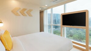 A hotel room with a large bed, a TV mounted on the wall, and a window with a city view. - Bloom Hotel - BKC Kalina (Mumbai)
