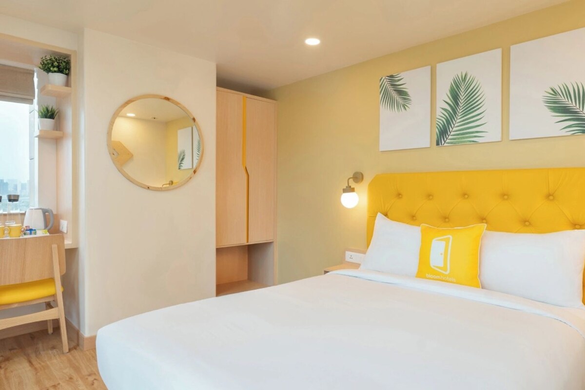 A hotel room with a bed, a desk, a chair, a round mirror, and wall art.