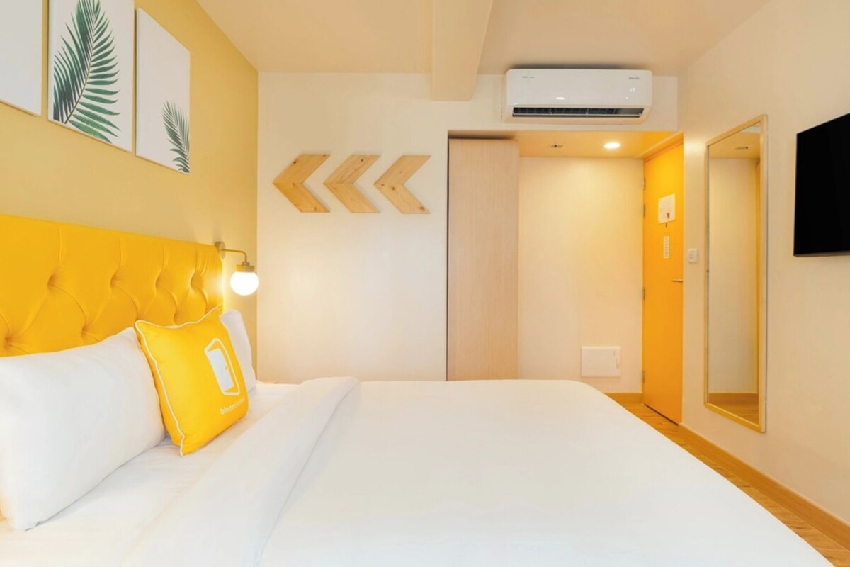 Habitación de hotel con cama, televisor de pantalla plana, equipo de aire acondicionado y puerta que da a otra habitación.