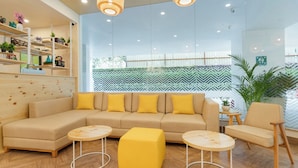 A modern living room with a sectional sofa, two round tables, and a yellow ottoman. - Bloom Hotel - BKC Kalina (Mumbai)