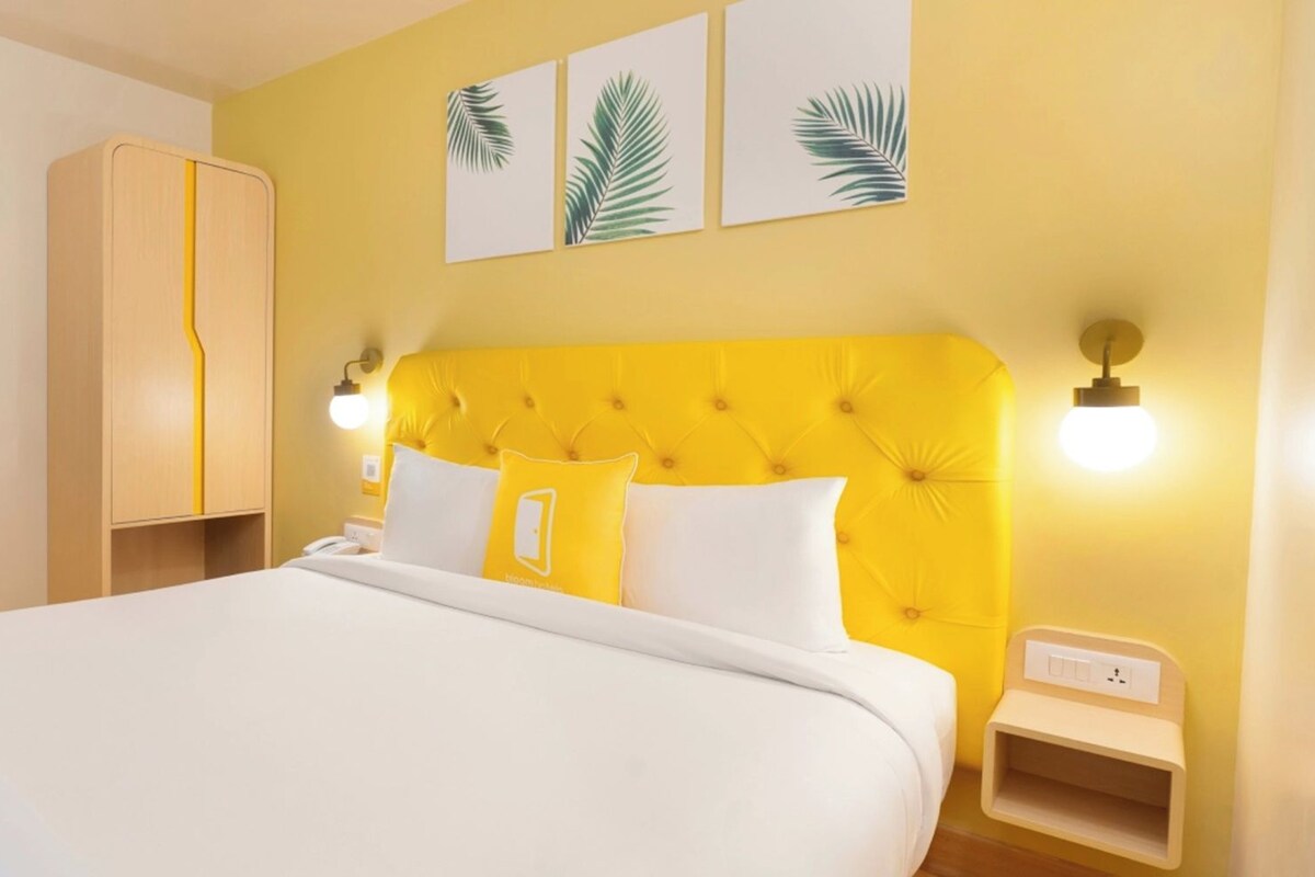 A hotel room with a large bed, a wardrobe, a bedside table, and wall-mounted lights.