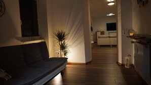 Ein modernes Wohnzimmer mit einem dunkelgrauen Sofa, einer Topfpflanze und Holzboden.