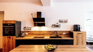 Eine moderne Küche mit Holzarbeitsplatte, integriertem Backofen, einer schwarzen Dunstabzugshaube, einem Spülbecken und einer Kaffeemaschine.