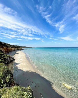 Uma praia com águas turquesa cristalinas, areal arenoso e um penhasco coberto de vegetação.
