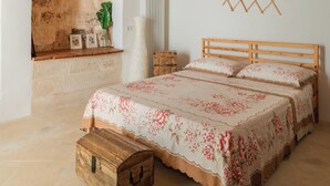 Ein Schlafzimmer mit Holzboden, Ziegelwand, Heizkörper, einer hölzernen Truhe und einem Bett mit Blumenmuster-Bettwäsche.