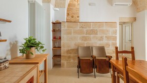 Ein gemütliches Zimmer mit Steinwand, Heizkörper, Holztisch, Stuhl und einer Topfpflanze.
