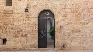 Ein Steinhaus mit einem schwarzen, bogenförmigen Eingang, einem kleinen Fenster mit grünem Rollo und einem Schild mit der Aufschrift '32' über der Tür.