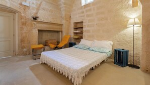 Ein Schlafzimmer mit Bett, Sessel, Lampe, Kamin und Steinwänden.