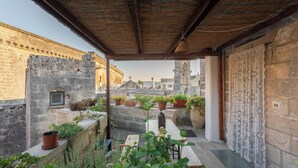 Un espace extérieur aménagé avec des sièges, abrité par un toit, doté de murs en pierre, de plantes en pot et offrant une vue sur le paysage urbain.