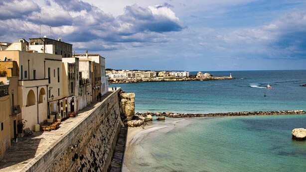 Une ville côtière dotée d’un rempart en pierre, de bâtiments et offrant une vue dégagée sur la mer.