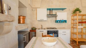 Une petite cuisine équipée d’une cuisinière à gaz, d’un évier et d’un four encastré. On y trouve une étagère en bois avec des serviettes et une plante en pot.
