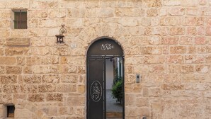 Un bâtiment en pierre avec une entrée arquée noire, une petite fenêtre avec des volets verts et un panneau portant le numéro « 32 » au-dessus de la porte.