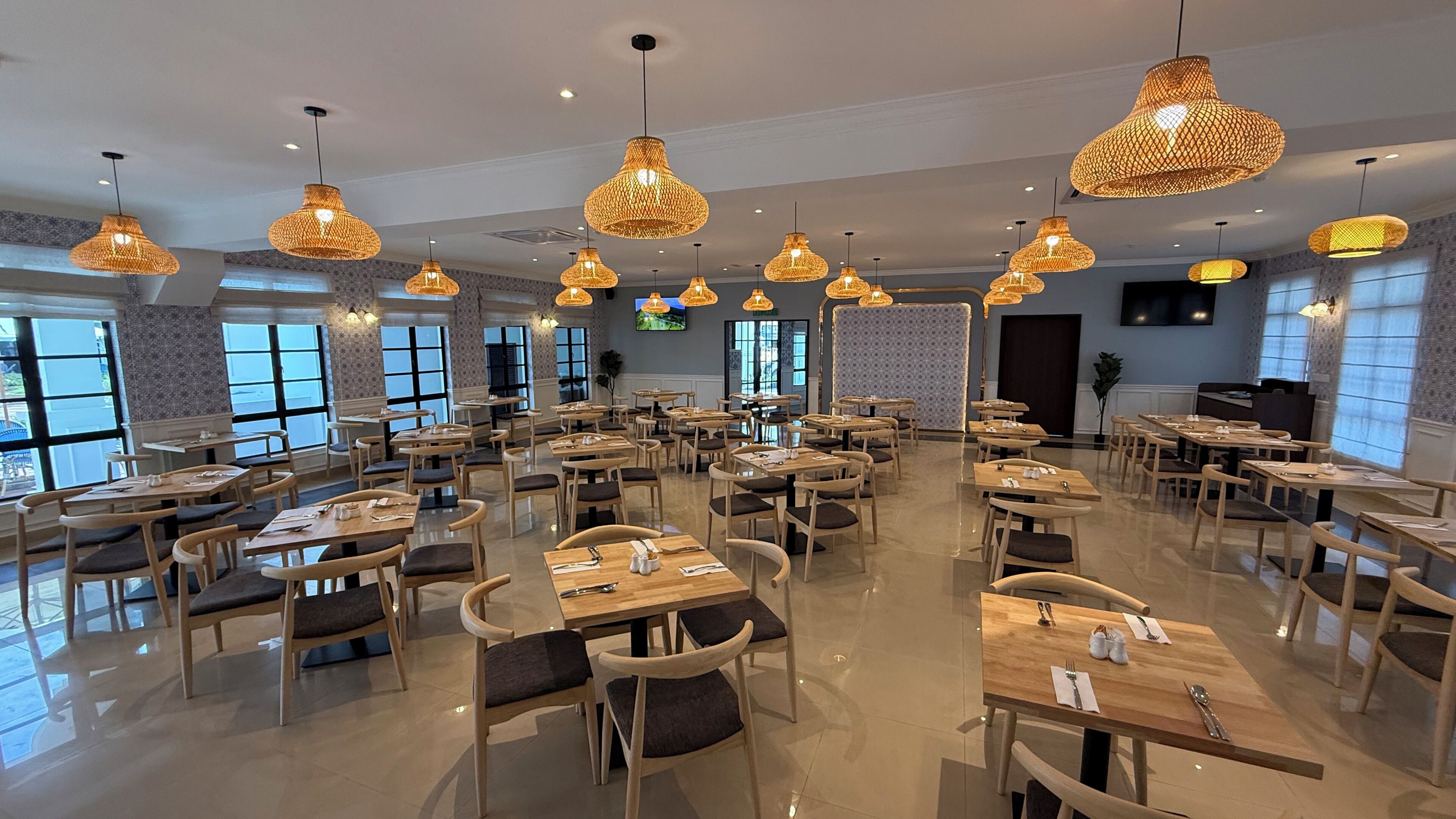 A spacious dining area with multiple tables and chairs, large windows, and hanging wicker lamps.