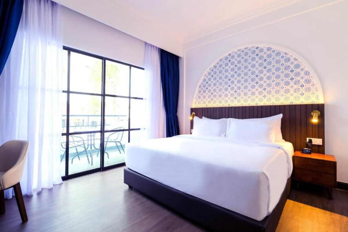 Une chambre d’hôtel avec un grand lit, une chaise, une table de chevet et une vue sur un balcon aménagé avec du mobilier d’extérieur.